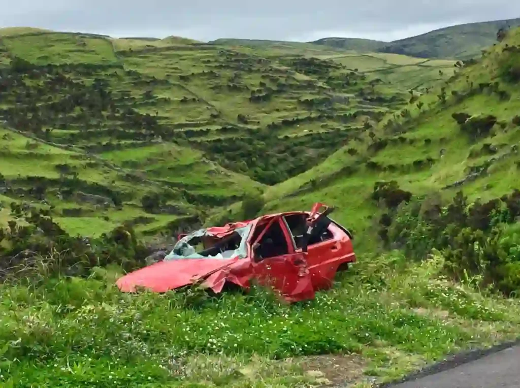 A red car with a crushed front and shattered windows sits abandoned on a grassy roadside crash site—ideal for ICBC kinesiology active rehab near me in Vancouver & Kitsilano, offering strength and conditioning to improve movement biomechanics after vehicle accidents.