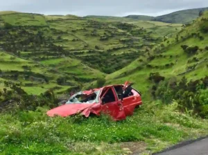 A red car with a crushed front and shattered windows sits abandoned on a grassy roadside crash site—ideal for ICBC kinesiology active rehab near me in Vancouver & Kitsilano, offering strength and conditioning to improve movement biomechanics after vehicle accidents.